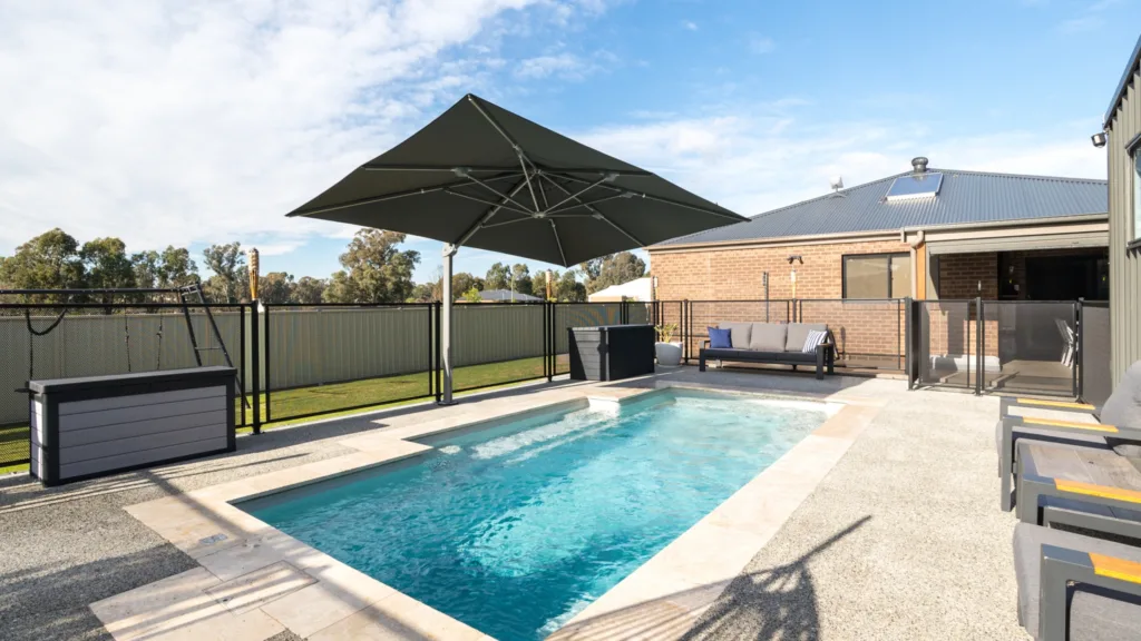 Outdoor pool with umbrella, lounge seating, and sunny yard
