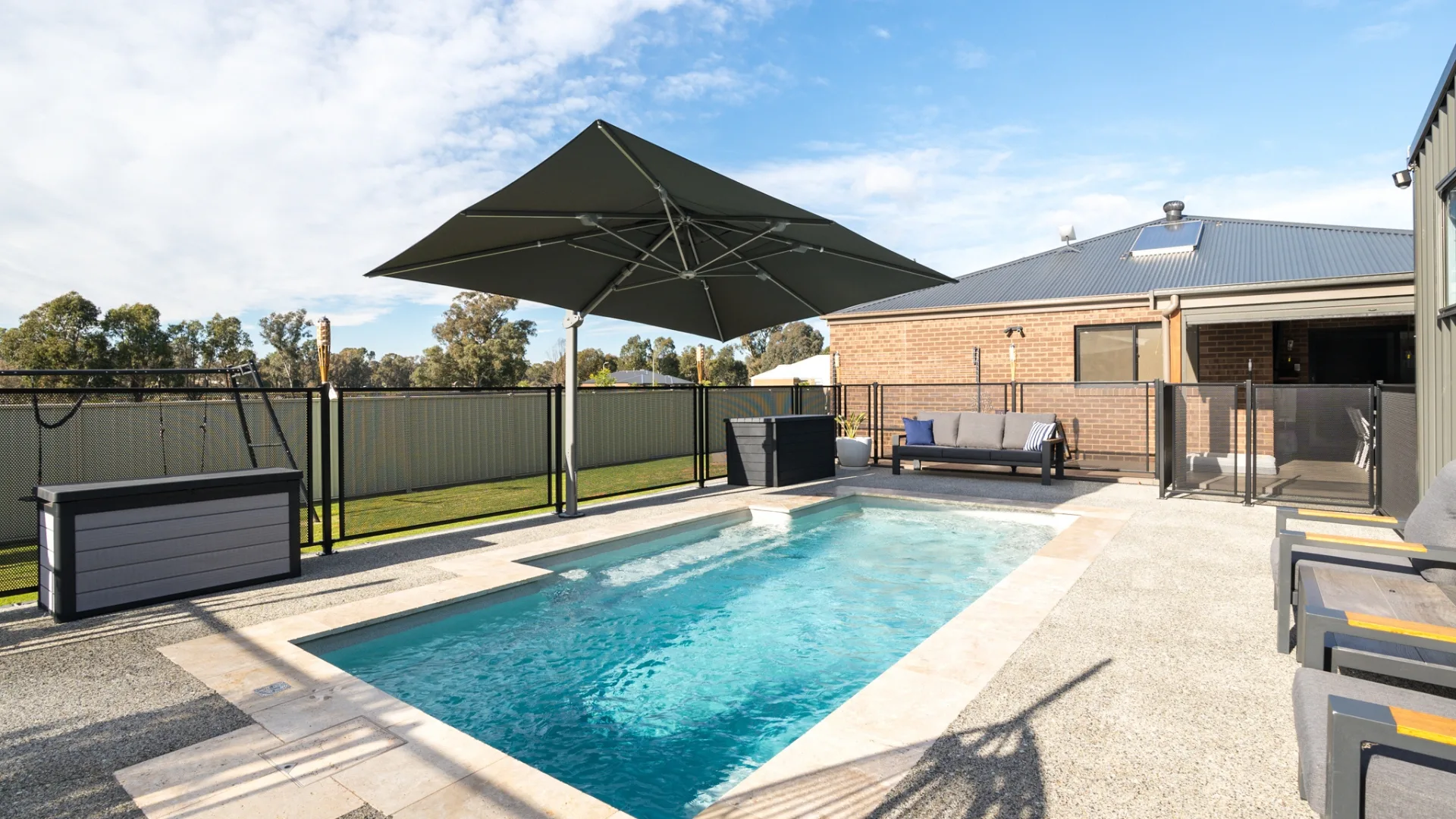 Outdoor pool with umbrella, lounge seating, and sunny yard