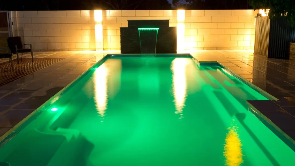 Narrow backyard pool beside house and dark fence