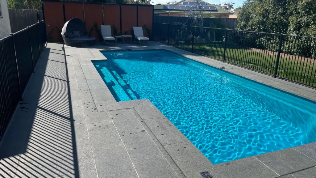 Modern backyard pool with loungers, umbrella, greenery