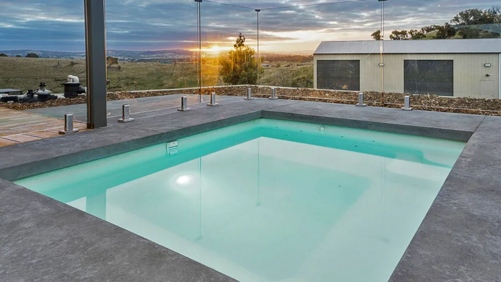 Modern outdoor pool with glass fence at sunset view