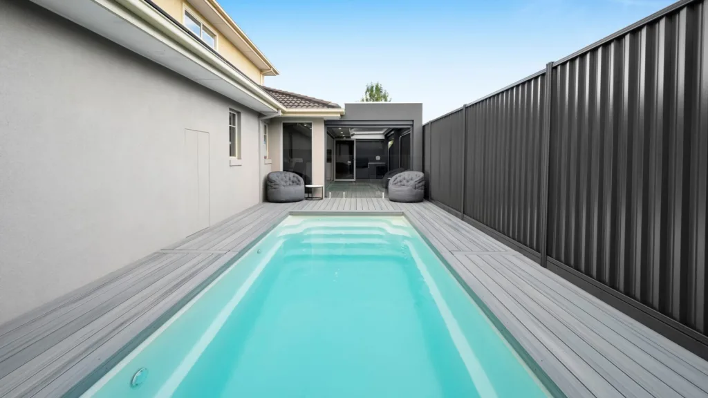 Narrow modern backyard pool with deck and seating area
