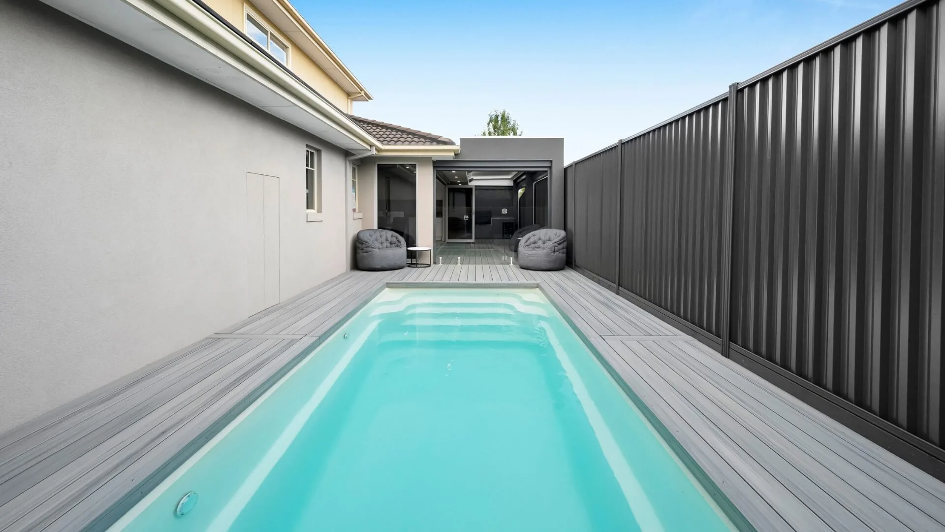 Narrow modern backyard pool with deck and seating area