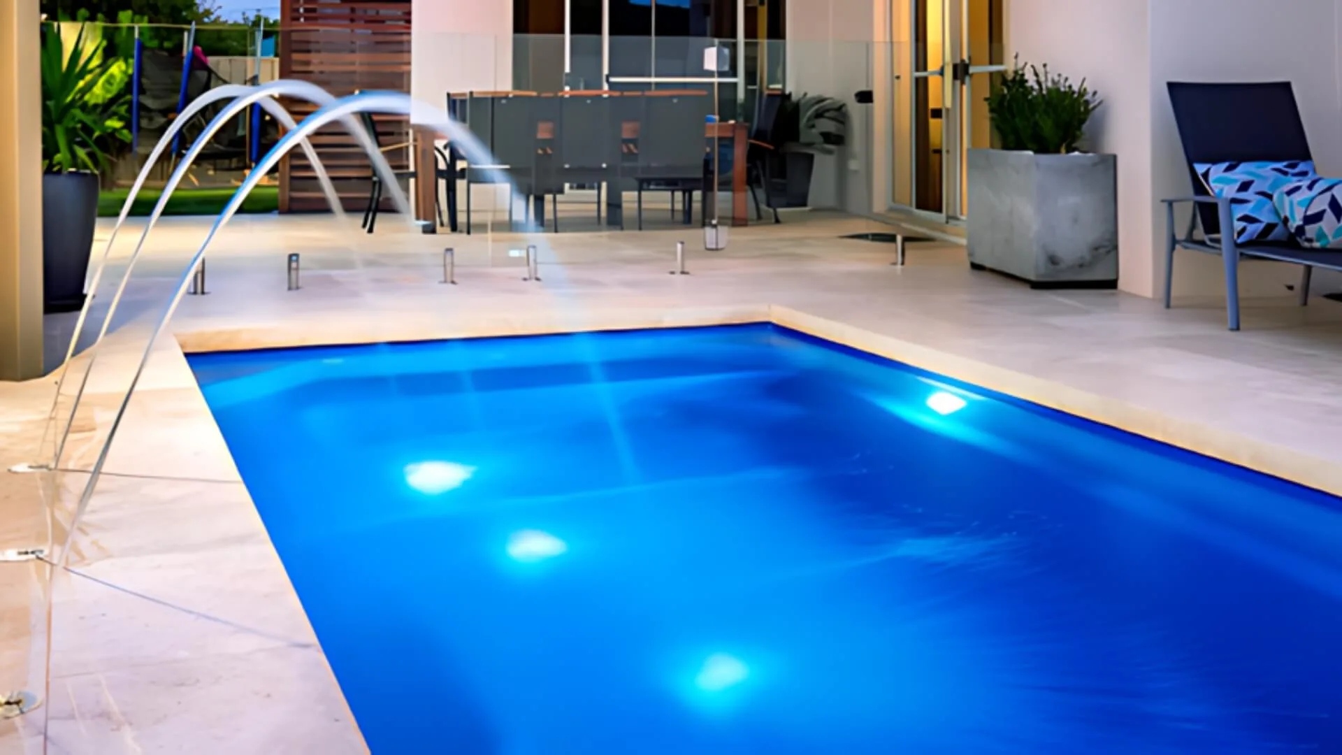 Modern backyard pool with lit water jets and patio seating